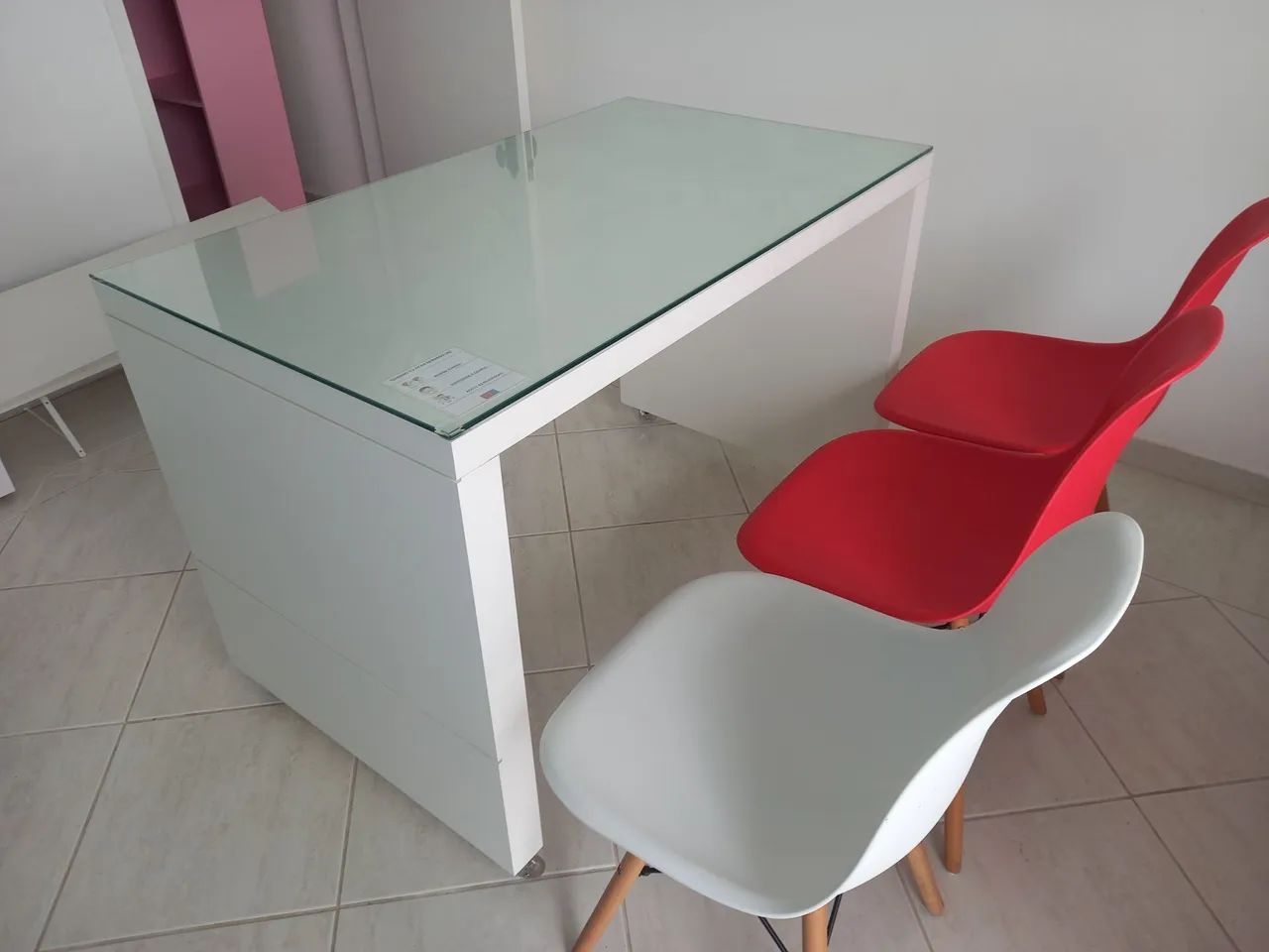Mesa de escritório com tampa de vidro e três cadeiras.