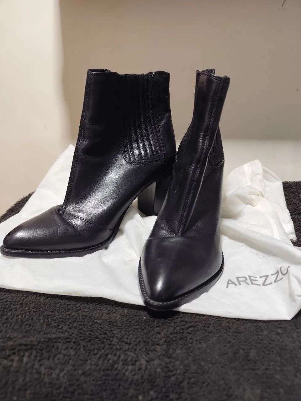 Bota preta de couro da marca Arezzo com bico fino e salto bloco.