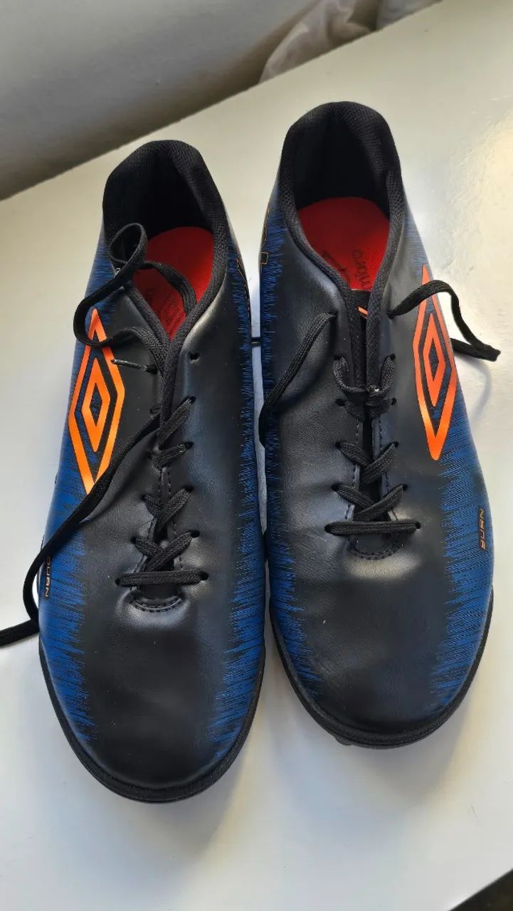 Chuteira Umbro modelo Burn Society, nas cores preto e azul, em ótimo estado de conservação