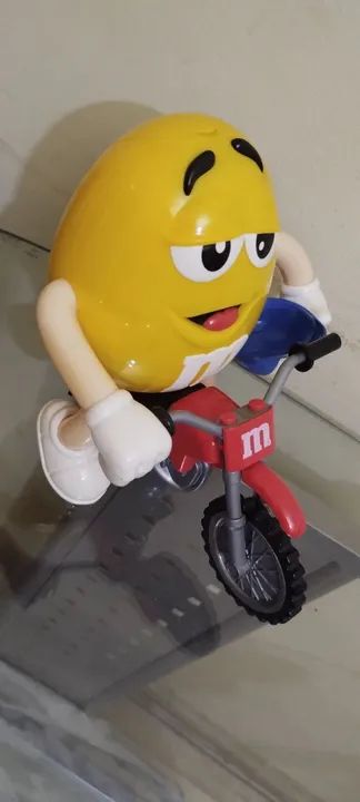 Boneco M&M amarelo de moto.