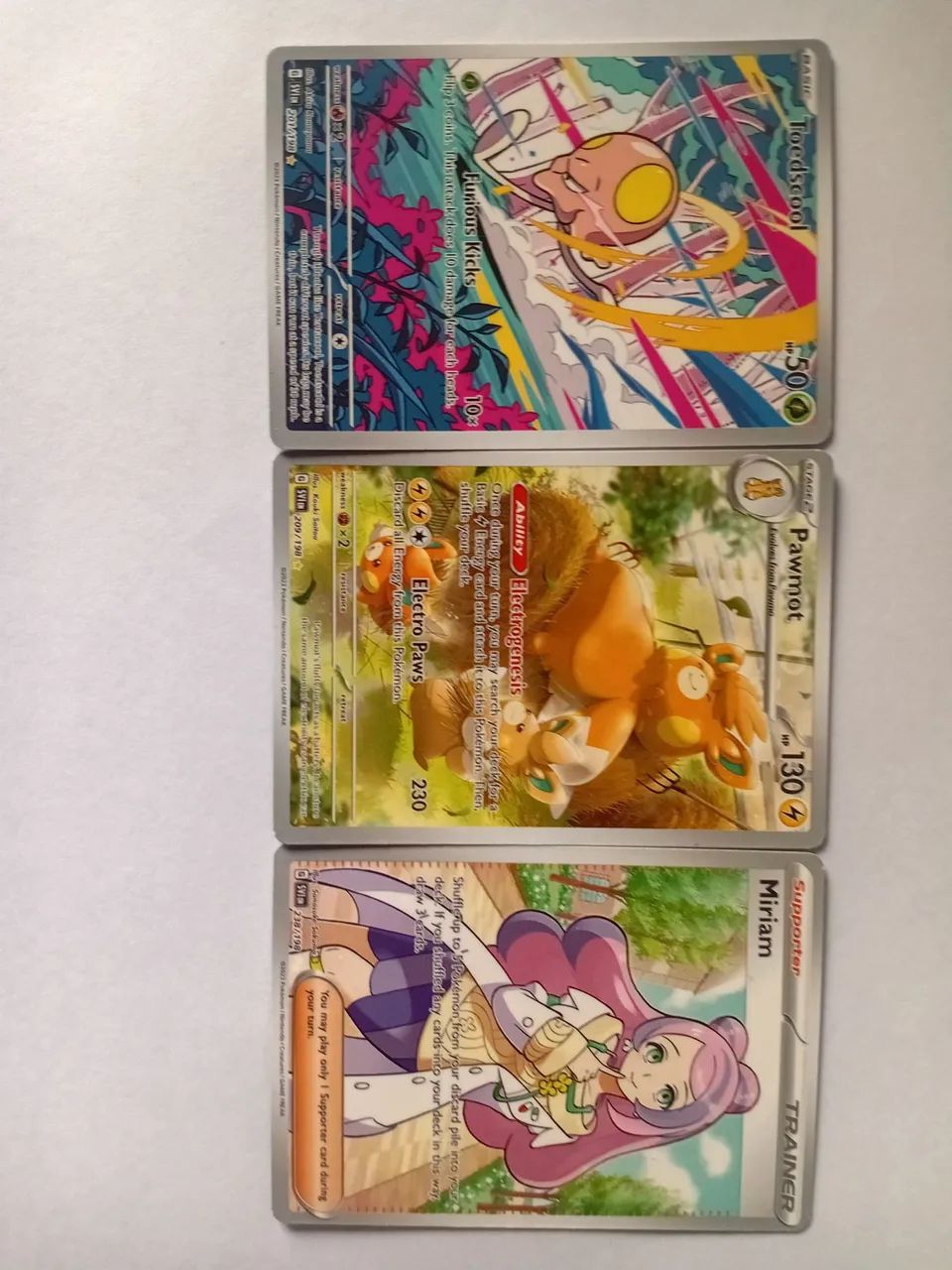Conjunto de três cards pokemon full art em inglês, dois Pokémons e um suporte 