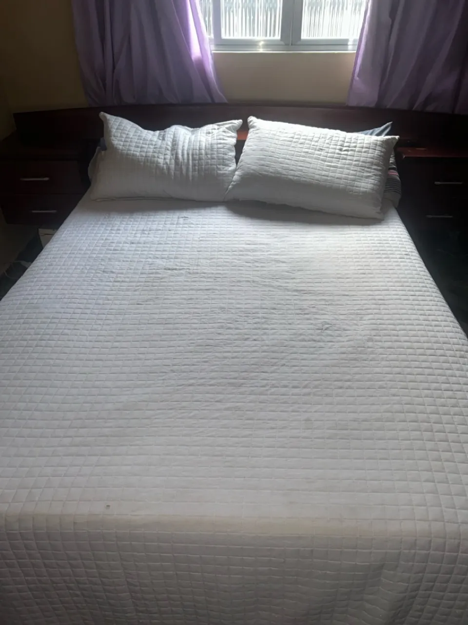 Cama de casal com cabeceira, baú e criado mudo.