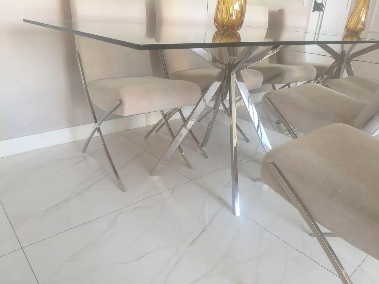 Mesa com base de inox com tampa de vidro, e quatro cadeiras.
