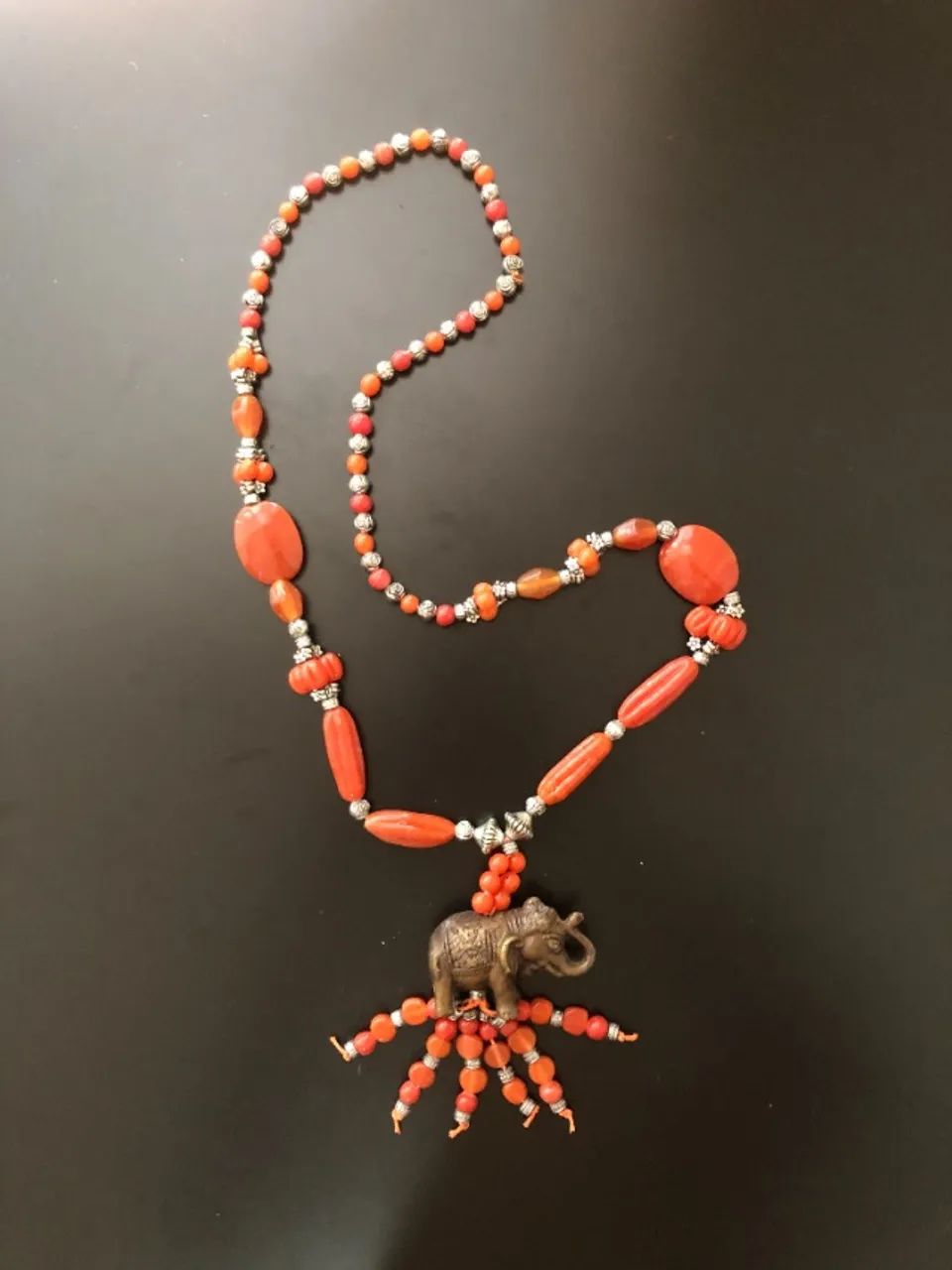 Colar longo laranja com pingente de elefante e franjas de contas.