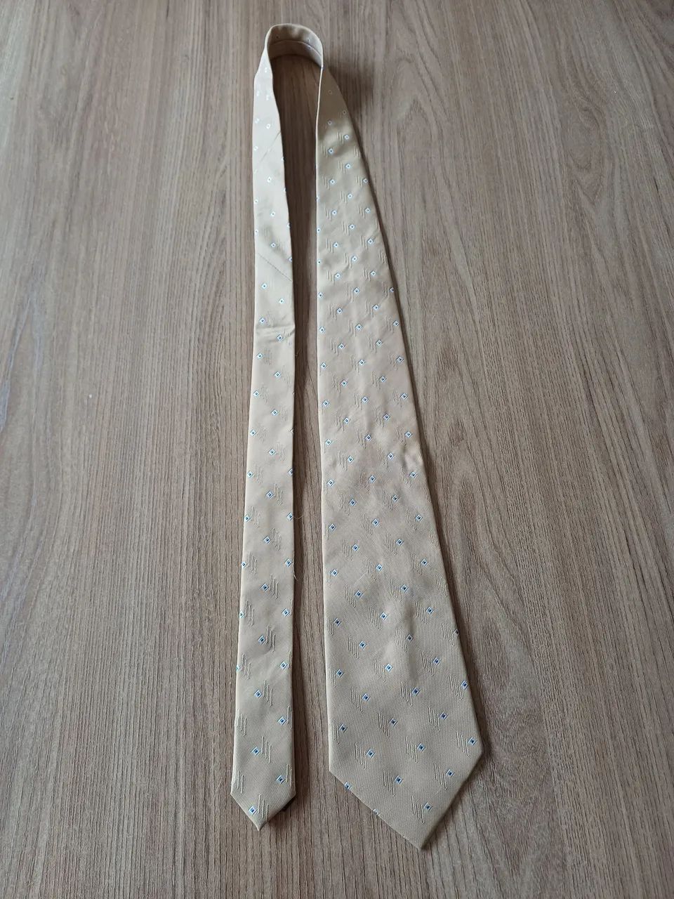 Gravata TNG dourada, com pontinhos branco e azul.