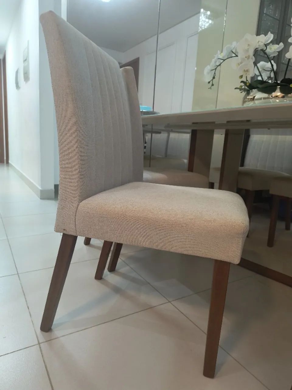 Cadeiras mesa de jantar coberta com linhão bege e feita de madeira na cor mel.