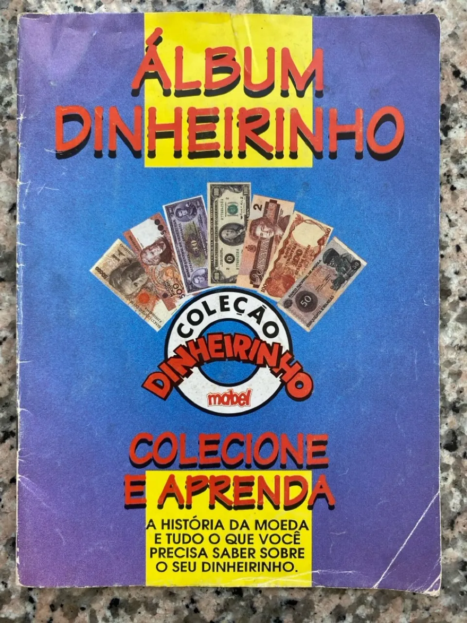 Álbum de figurinhas colecionável chamado Dinheirinho, da marca Mabel, lançado nos anos 90