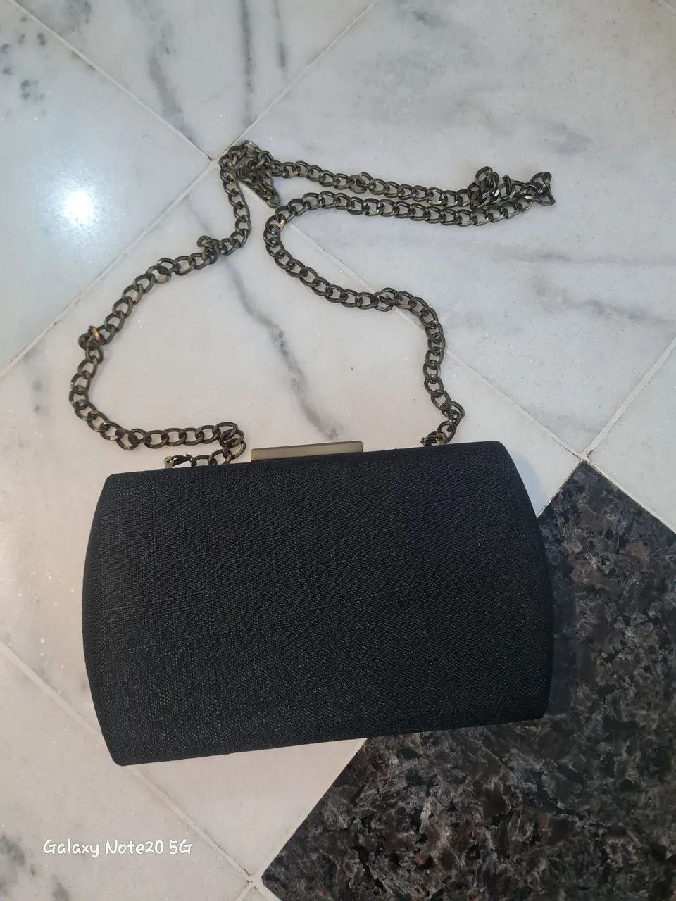 Bolsa de festa preta estilo clutch de tecido telado com alça de corrente metálica.