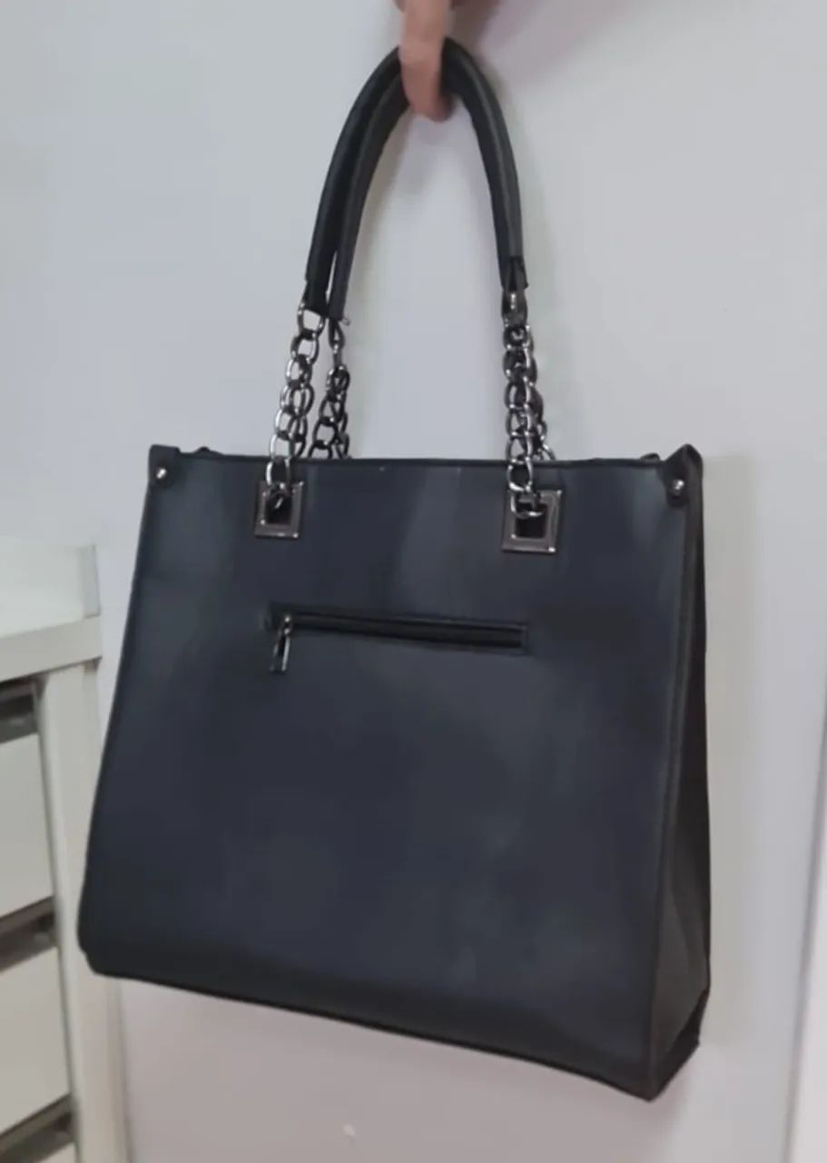 Bolsa preta de couro sintético, tamanho grande e com alça de couro e corrente. 
