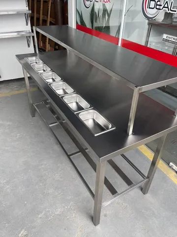Mesa industrial com condimentadora de bancada e prateleira de apoio. 