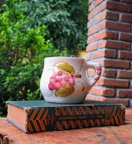 Caneca de faiança antiga pintada à mão com decoração de cachos de uva.