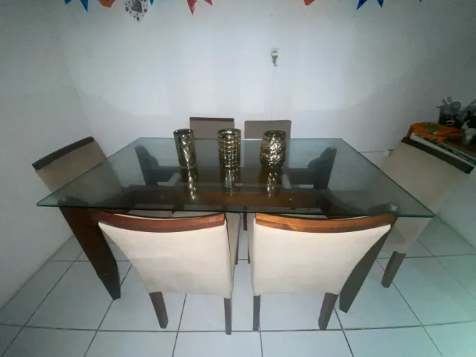 Mesa de vidro com 6 cadeiras com acabamento macio uma das cadeiras está sem cabeça 