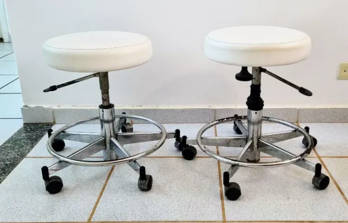 2 mochos odontológicos, em couro branco, estrutura cromada, com rodízios, sem encosto