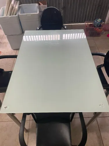 Mesa de vidro acompanhada com 4 cadeiras plásticas pretas