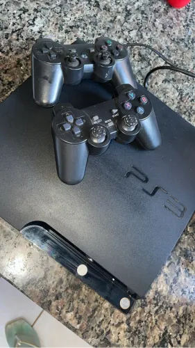 Vendo Ps3, bloqueado, acompanhando de dois controles, e mais de 5 jogos baixados