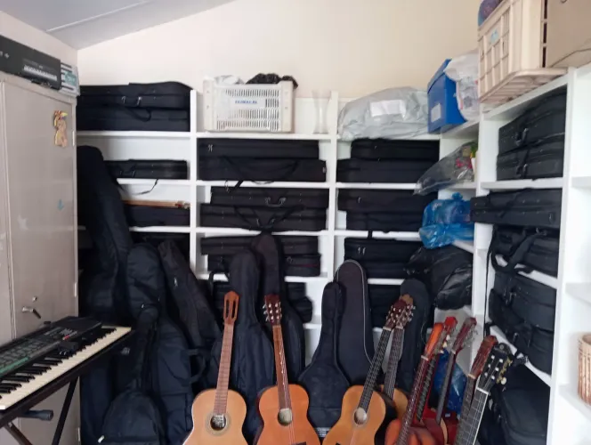 Vendo violão, violinos, flautas, estantes.