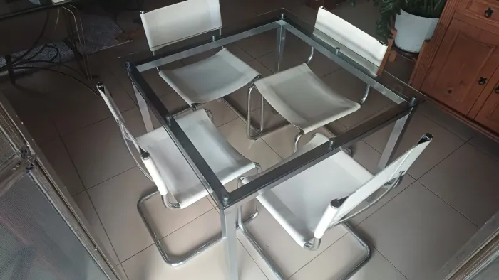 Mesa em aço, tampo de vidro, com quatro cadeiras com assento em couro legítimo.