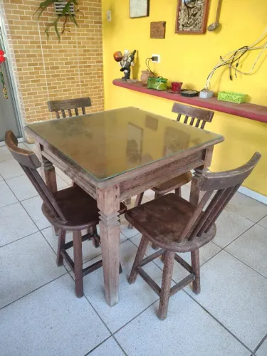 Mesa em Madeira com 4 Cadeiras, todas em madeira, com tampo de vidro para proteção.