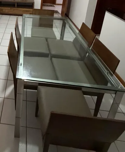 Mesa tampo de vidro e base em inox com 6 cadeiras de madeira e assento em corino bege. 