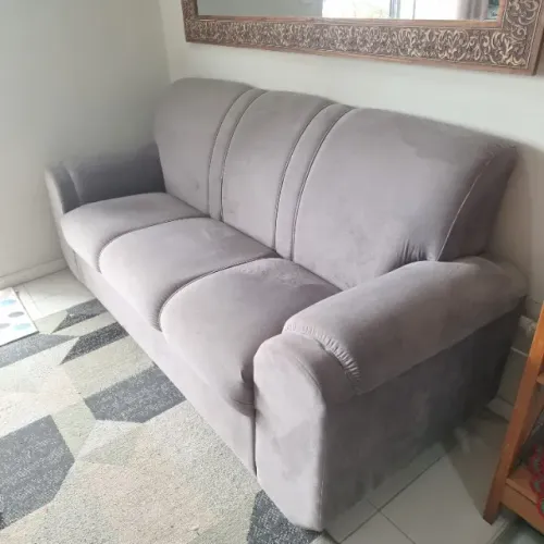 Sofá de três lugares em tecido tipo veludo cinza.