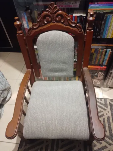 Poltrona antiga de madeira maciça, com braços, encosto estofado e entalhes decorativos.