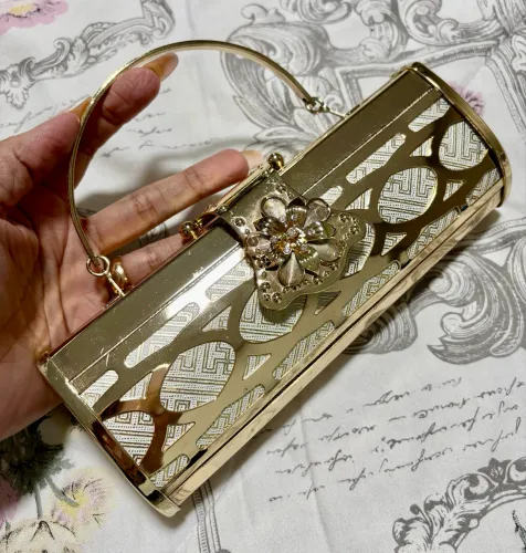 Bolsa clutch com alça e detalhes de acabamento em metal dourado.