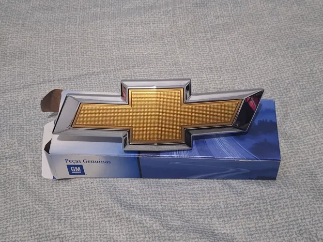 EMBLEMA GRAVATA GRADE DIANTEIRA GM CHEVROLET ONIX 2020/2025 COD: 26224695