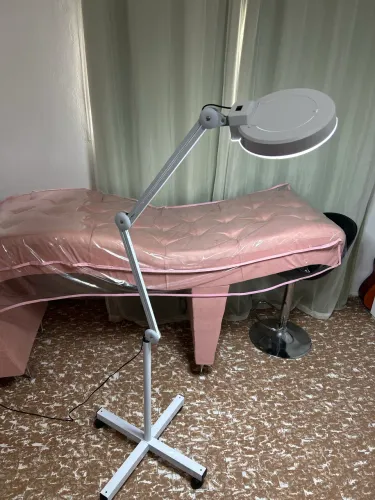 Luminária lupa articulada, e maca rosa estética profissional com cadeira giratória.