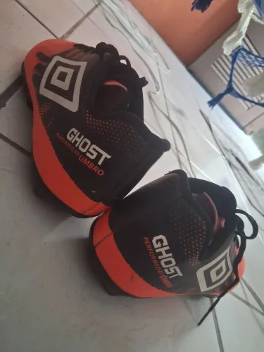 Chuteira Umbro Ghost, modelo de campo com travas, cor preta com detalhes laranja.