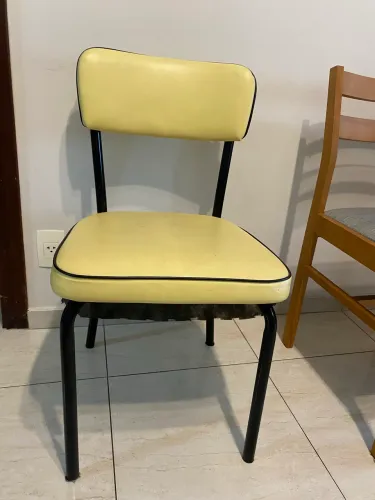 Cadeira estofada em amarelo, acabamento em preto e base metal.