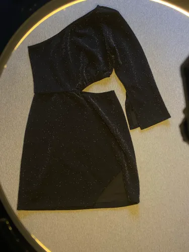 vestido preto com brilhos, um ombro só, detalhe na cintura e recortes na saia e manga.