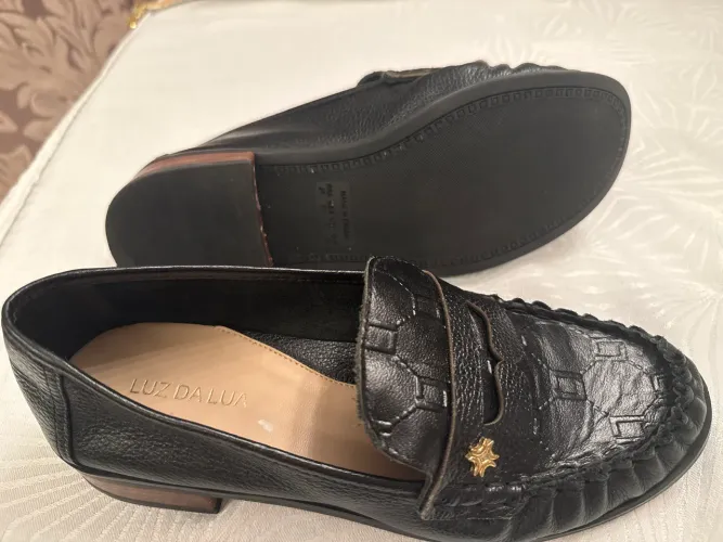 sapato mocassim loafer de couro preto com um detalhe dourado na parte superior.