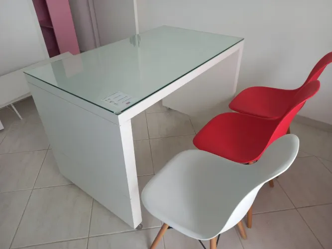Mesa de escritório com tampa de vidro e três cadeiras.