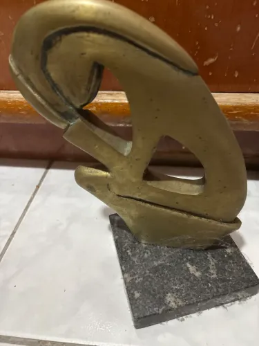 Escultura abstrata em metal dourado sobre base de pedra