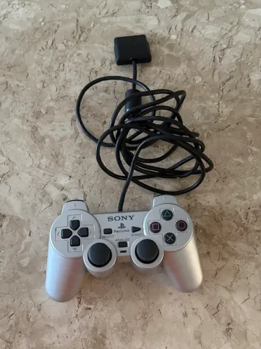 Controle original Sony PlayStation, na cor prata, com conexão por cabo.