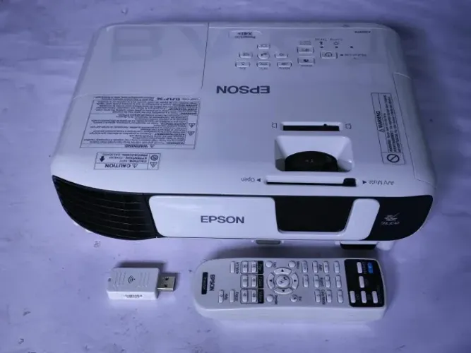Projetor Epson PowerLite X41+ acompanhado de seu controle remoto e um adaptador Wi-Fi USB