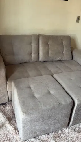 Sofá cinza revestido em tecido suede com um puff modular na parte frontal