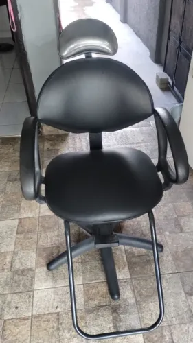 uma cadeira preta de salão de beleza com regulagem de altura e apoio para os pés.