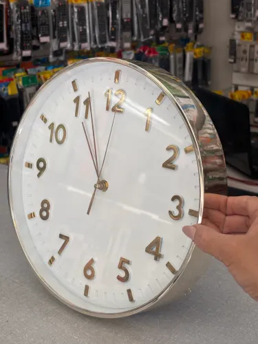 relógio de parede moderno com visor branco e números tridimensionais em tom dourado.