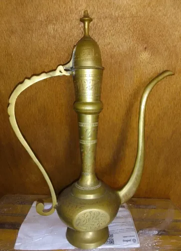 Bule Indiano de metal dourado. Base redonda. Corpo com duas partes achatadas. Alça vazada