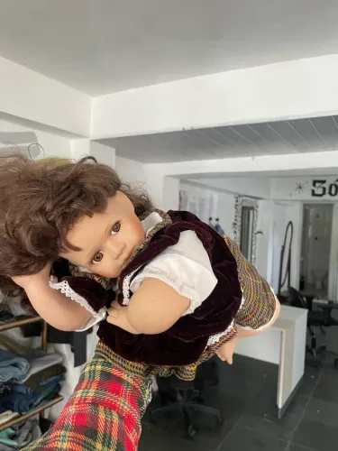 boneca de porcelana vintage com cabelo castanho e roupas de tecido xadrez deitada 