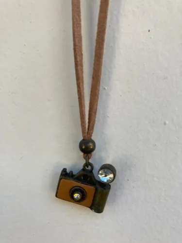 Colar de couro com pingente de máquina fotográfica.