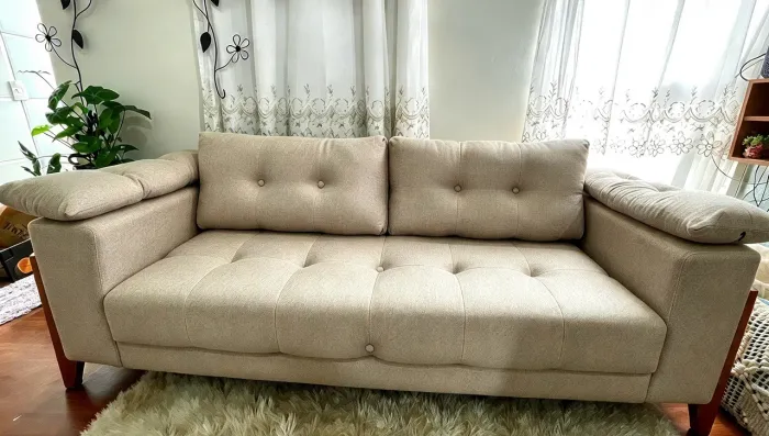 Um sofá de 3 lugares, com design clean e tecido bege, ideal para ambientes aconchegantes. 