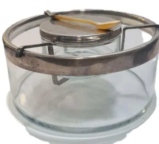 Porta Caviar, composto por uma estrutura de vidro incolor e guarnições em metal prateado. 