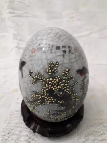 Ovo decorativo oriental em cerâmica esmaltada apoiado em base de madeira.