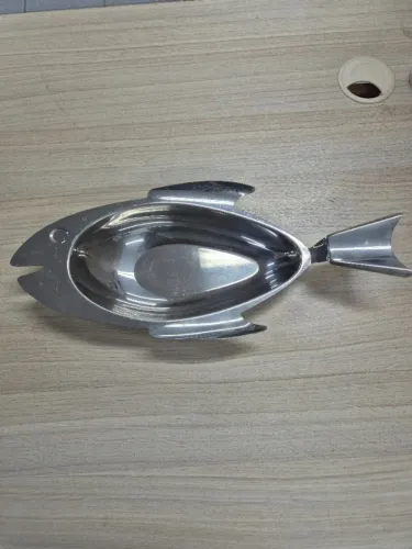 Travessa de aço inoxidável em formato de peixe, utilizada para servir alimentos. 