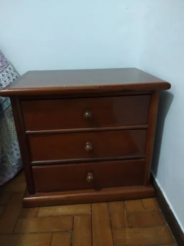 mesa de cabeceira de madeira maciça com três gavetas e puxadores redondos.