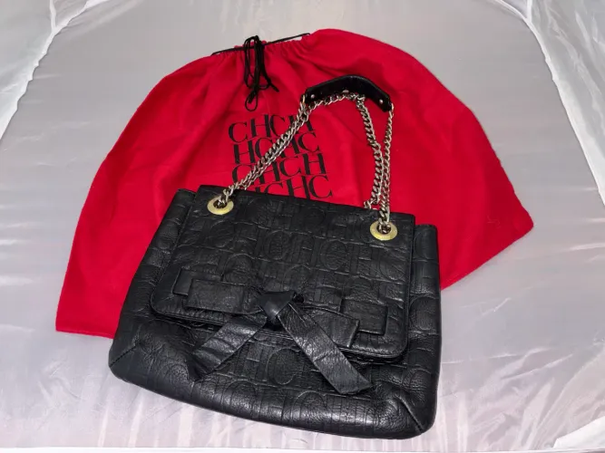 bolsa Carolina Herrera modelo Audrey, em couro preto, alça de corrente e laço frontal.