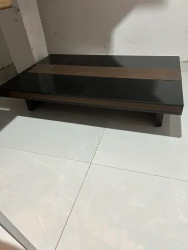 mesa de centro de design moderno com tampo de vidro preto e estrutura amadeirada.