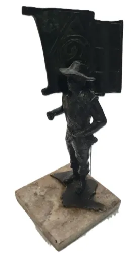 Estátua representa um soldado ou bandeirante com uma bandeira ( faltando o mastro )  e esp